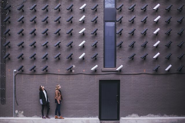 A large wall covered with security cameras, with two women looking at it.